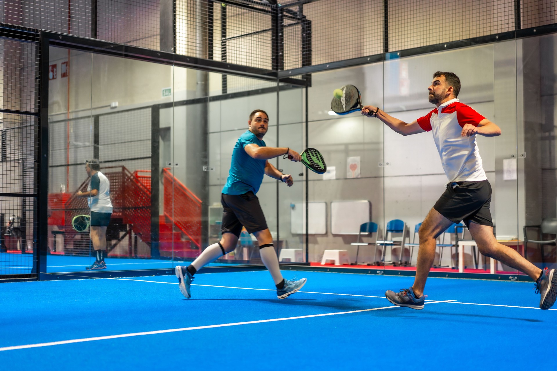 Friends playing paddle tennis energetically in an indoor court